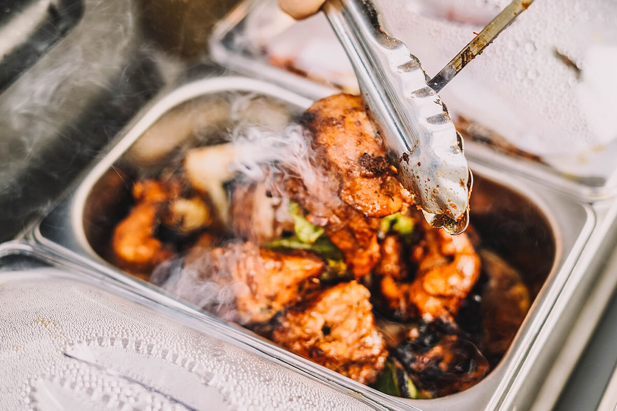 Silver tongs pick up cooked food from dish